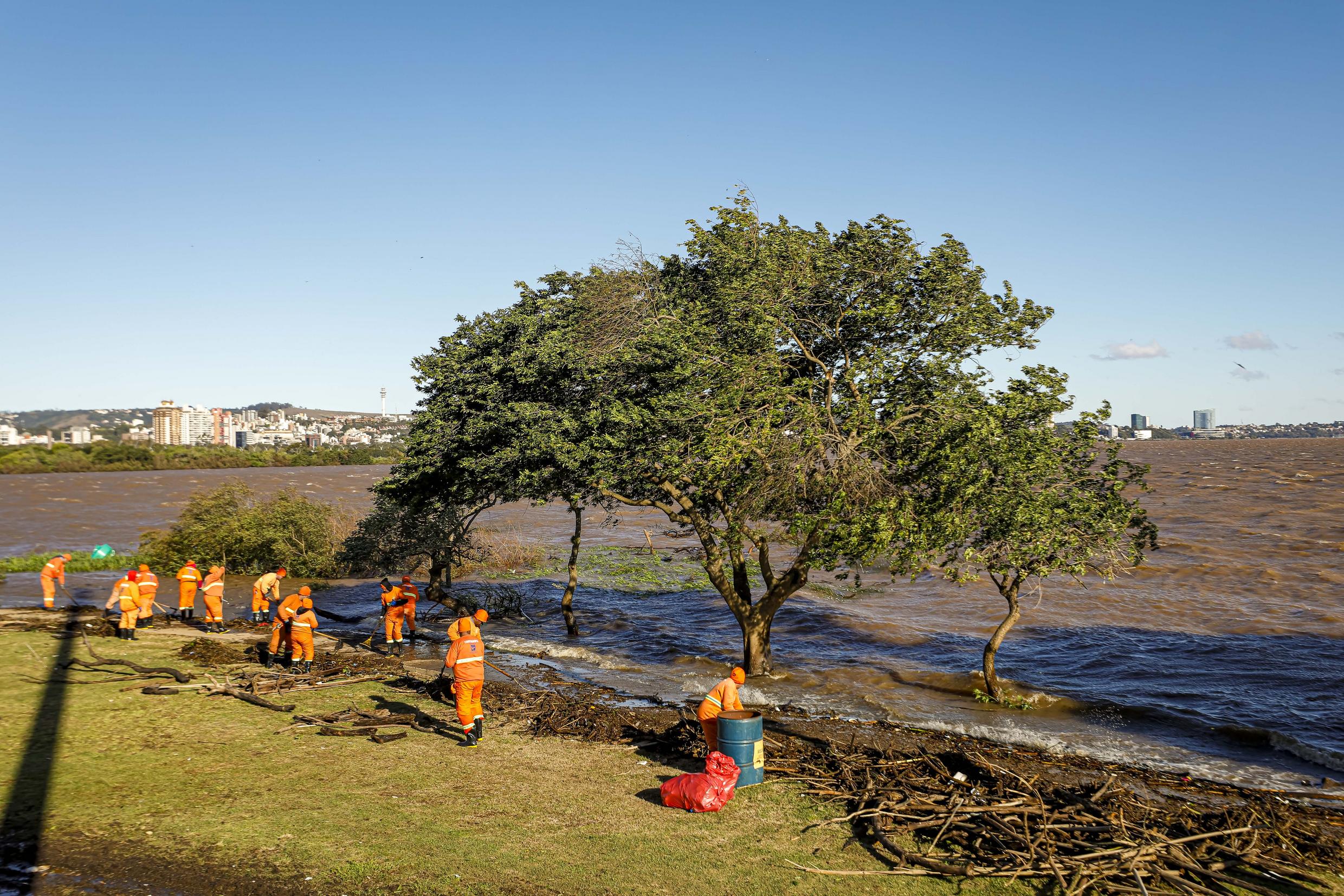 A imagem mostra garis realizando uma ação especial de limpeza na Orla do GuaÃba após as chuvas que atingiram a cidade.